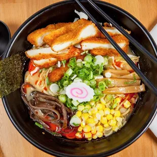 a bowl of ramen with tofu, corn, broccoli, and other vegetables