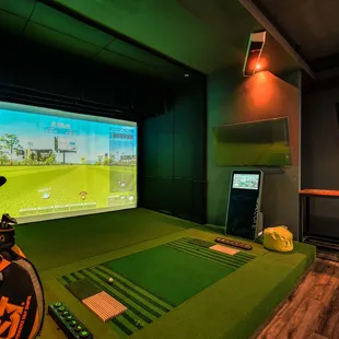 a golf simulator with a television and a golf bag
