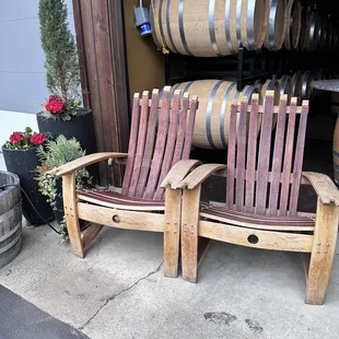 two wooden chairs with wine barrels in the background