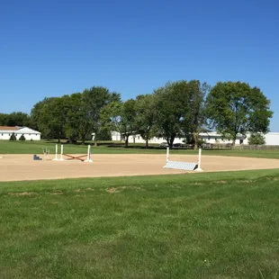 outdoor all-weather arena in the foreground, indoor heated arena is at the back  of the stables