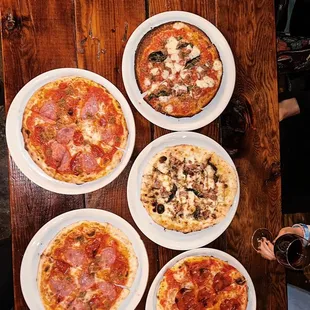 four pizzas on plates on a wooden table