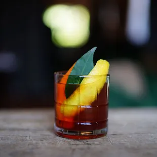 a glass of cocktail with an orange garnish