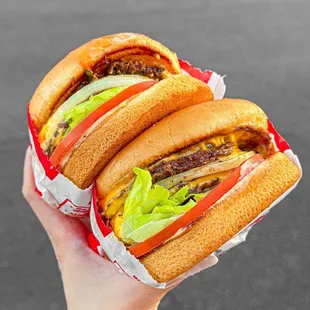 ows a hand holding two hamburgers