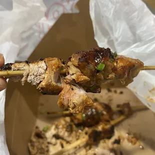 a hand holding a skewer of chicken