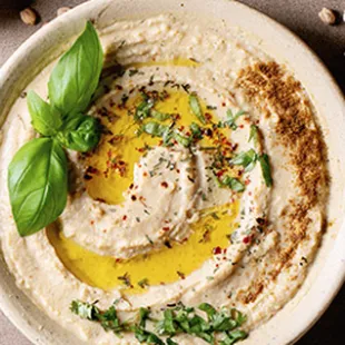 a bowl of hummusle with a sprig of basil