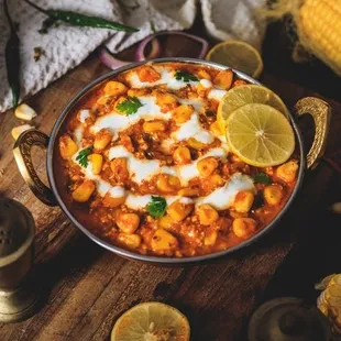 a bowl of chick curry with a side of corn and lemons