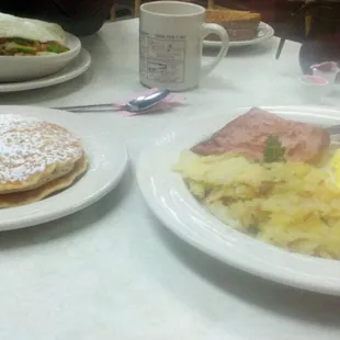 a breakfast of pancakes, eggs, ham, and hash browns