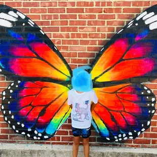 My son taking a photo in front of butterfly mural outside.