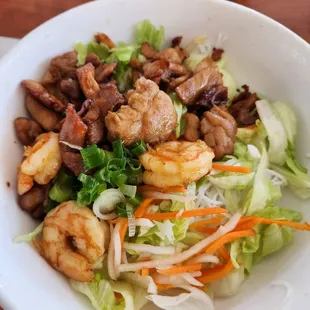 a white bowl of food with shrimp, lettuce and carrots