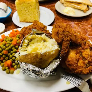 Fried chicken with a baked potato and peas and carrots with cornbread.