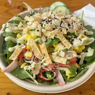 Salad poke bowl with crab salad, spinach, wontons, sesame seeds, mango, pineapple, green onions, cucumbers, carrots, and more.