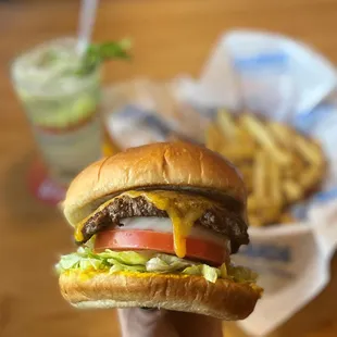 a hand holding a cheeseburger and fries