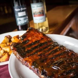 a plate of ribs, potatoes and a bottle of wine