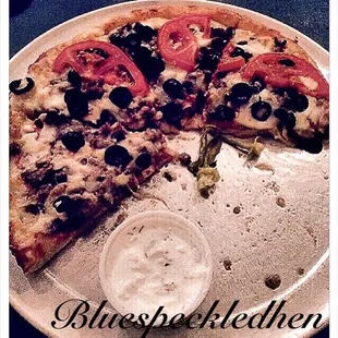 A small Greek pizza with a side of tzatziki.