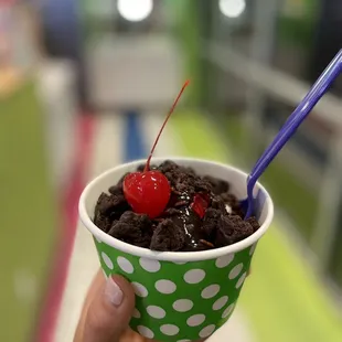 a person holding a cup of ice cream with a cherry on top