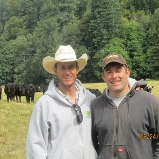 two men standing in front of a herd of cows