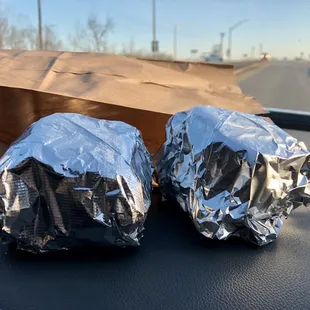 two wrapped sandwiches on the dashboard of a car