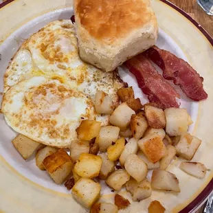 Breakfast plate with eggs cooked over medium, bacon and potatoes.