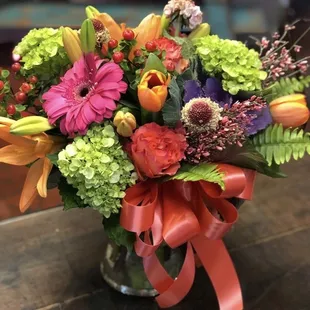 Beautiful and colorful.  Garden design of fresh hydrangeas, roses, tulips, gerbera daises, lilies, and berries in a clear gathering vase.