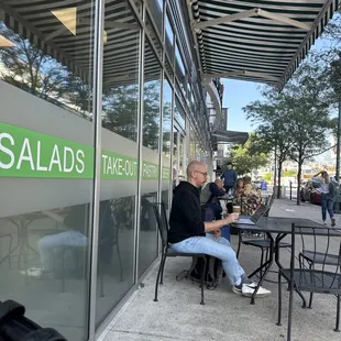 a man sitting at a table outside a salads takeout