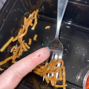 a hand holding a fork over a tray of food