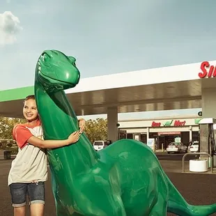 a young girl standing next to a green dinosaur statue
