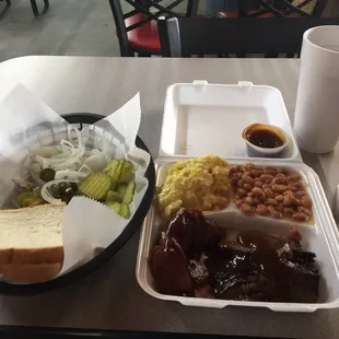 Beef brisket and sausage plate with potato salad and baked beans, with a side of jalapenos, onions, pickles and bread.