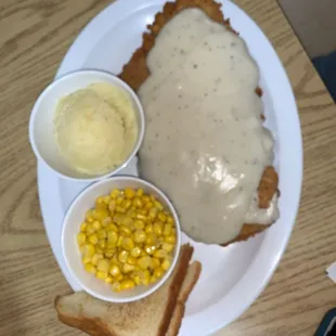 a plate of fried chicken with gravy, corn and mashed potatoes
