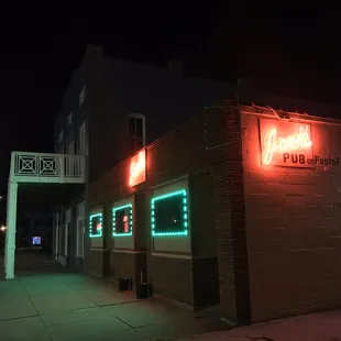 Neon beckons you! Parking lot against side of building.
