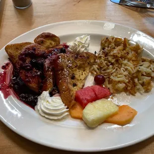 a plate of french toast with fruit and whipped cream