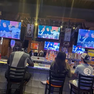 people sitting at a bar watching tvs