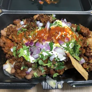 Nachos Locos with Al Pastor pork, pinto beans, queso, sour cream, cilantro, onion, and hot sauce! They make the chips in house!