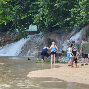 a group of people standing on a beach near a waterfall