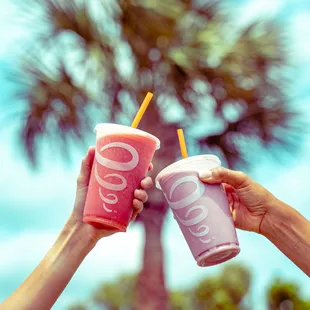 two people holding up two cups of smoothie