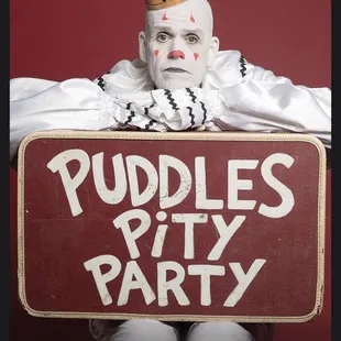 a clown holding a sign that says puddles party
