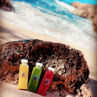 three bottles of juice on a rock on the beach