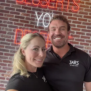 Owners Bethany &amp; Colt Nelms in front of company motto, "Desserts You Deserve" sign