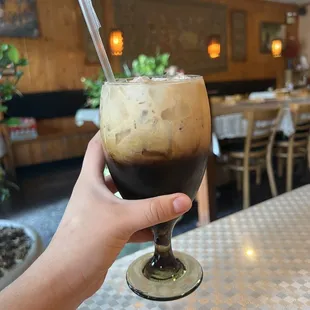 a hand holding a glass of iced coffee