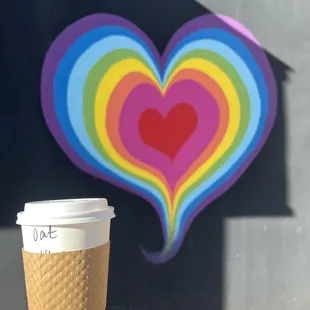 a hand holding a coffee cup in front of a mural of a heart