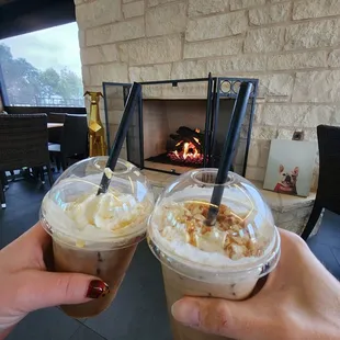 two people toasting drinks in front of a fireplace