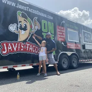 a man and a little girl standing in front of a food truck
