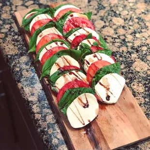 a wooden cutting board topped with sliced tomatoes and mozzarella