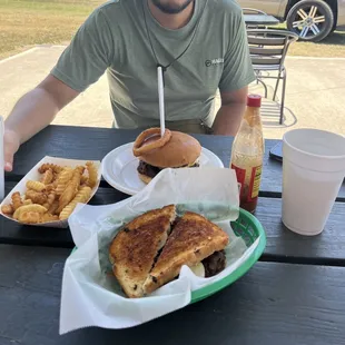 a man sitting at a picnic table with a sandwich and french fries