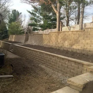 Two levels of retaining walls creating garden beds.  Surrounding, protected by over-scallop, semi-private, wood fence in Lincoln, NE.