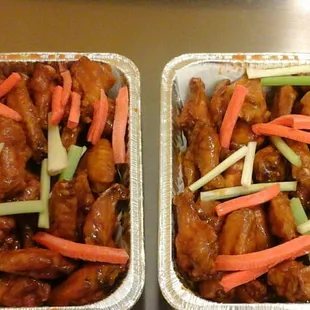 two trays of chicken wings with carrots and celery