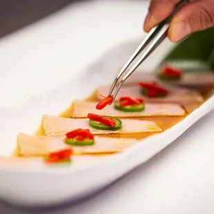 a hand holding chopsticks over a dish of food