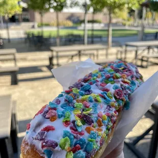 a hand holding a donut with sprinkles