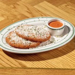 two powdered sugar donuts on a plate with dipping sauce