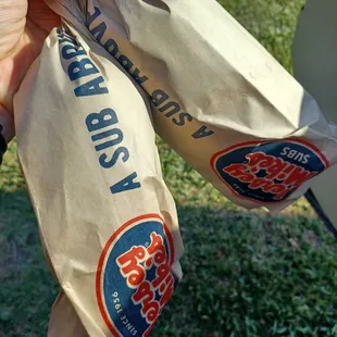 a person holding a bag of subs