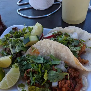 two tacos on a plate with lime wedges